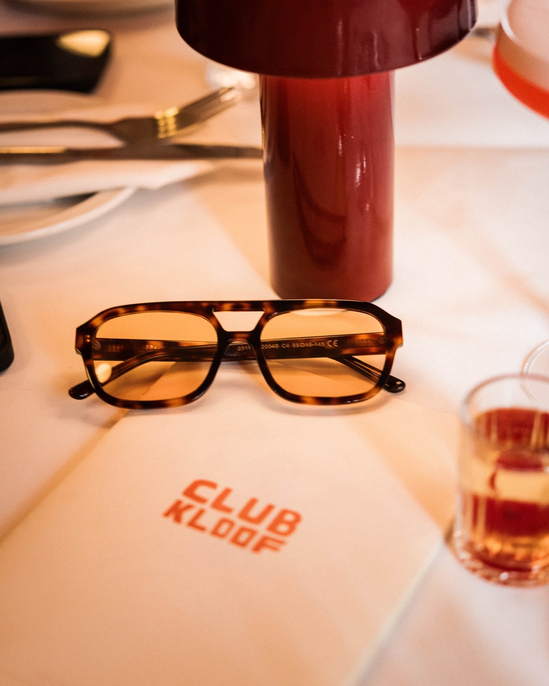 rectangular aviator sunglasses with tortoiseshell acetate frames and amber-tinted lenses on a dinner table