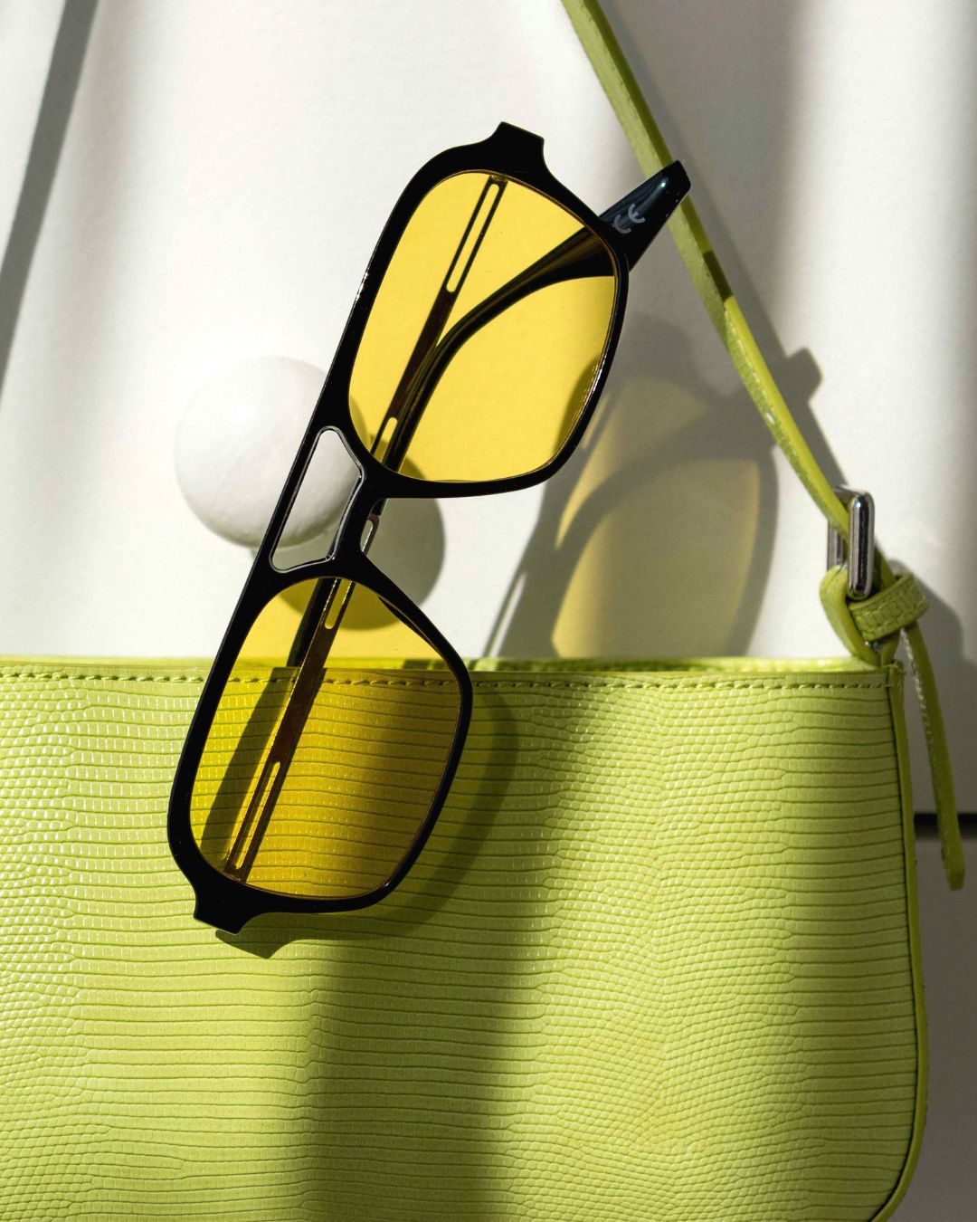 flat lay of aviator sunglasses with yellow lenses and handbag